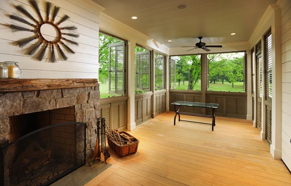 Cozy indoor porch in a Mossy Ridge constructed home, highlighting a majestic stone fireplace as the centerpiece. This serene space combines rustic charm with modern sustainability, featuring comfortable seating and panoramic windows that invite natural light and views of the outdoors.